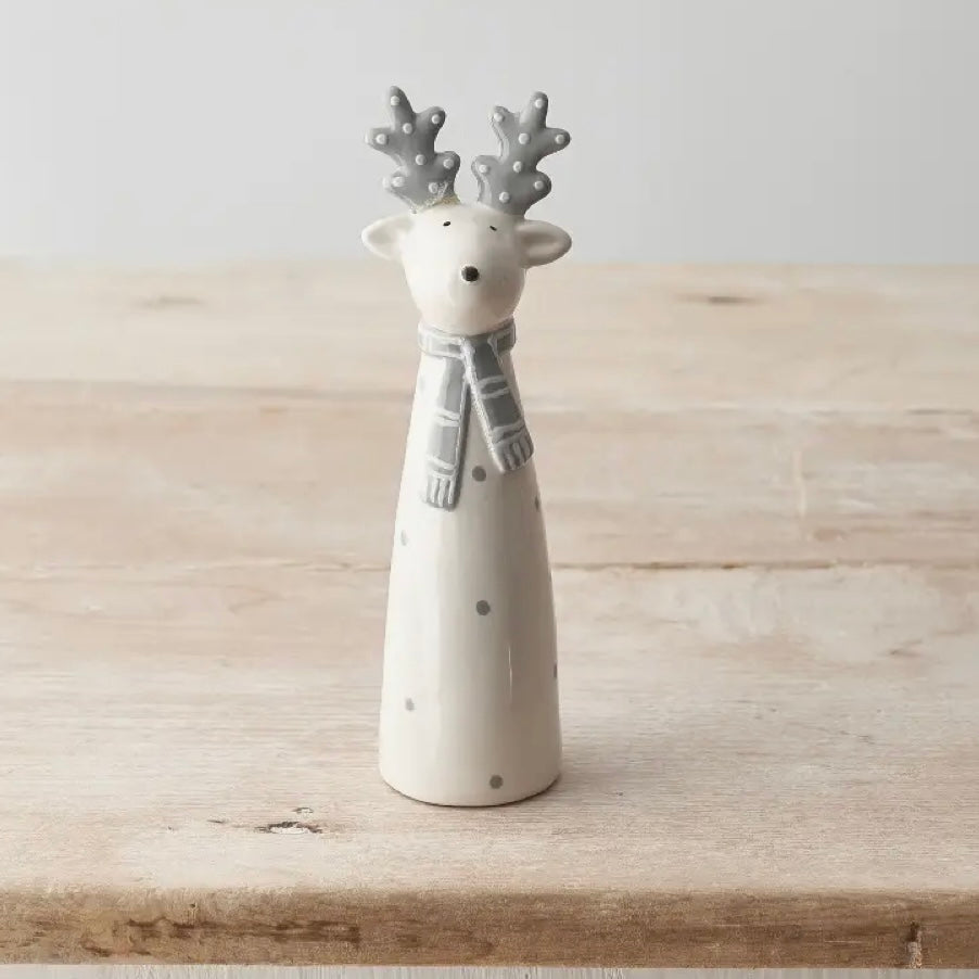 Ceramic reindeer figurine with gray antlers and scarf on a wooden surface