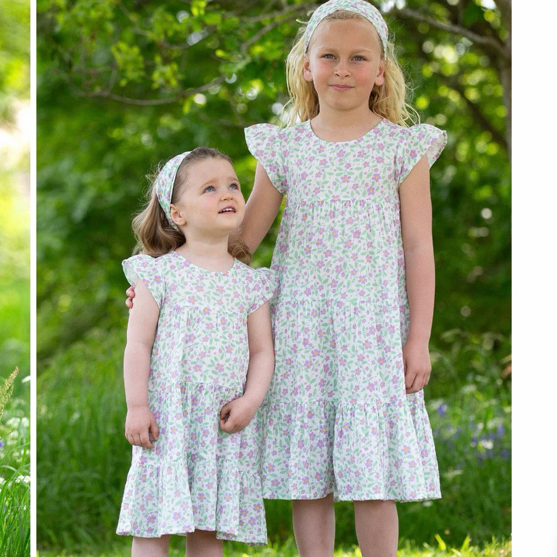 Two young girls wearing matching floral print dresses and matching headbands, standing outdoors in a grassy garden setting.
Children's clothing
Dress
Kids clothes
Floral dress
Occasion dress
GOTS Certified fabrics
Kite clothing