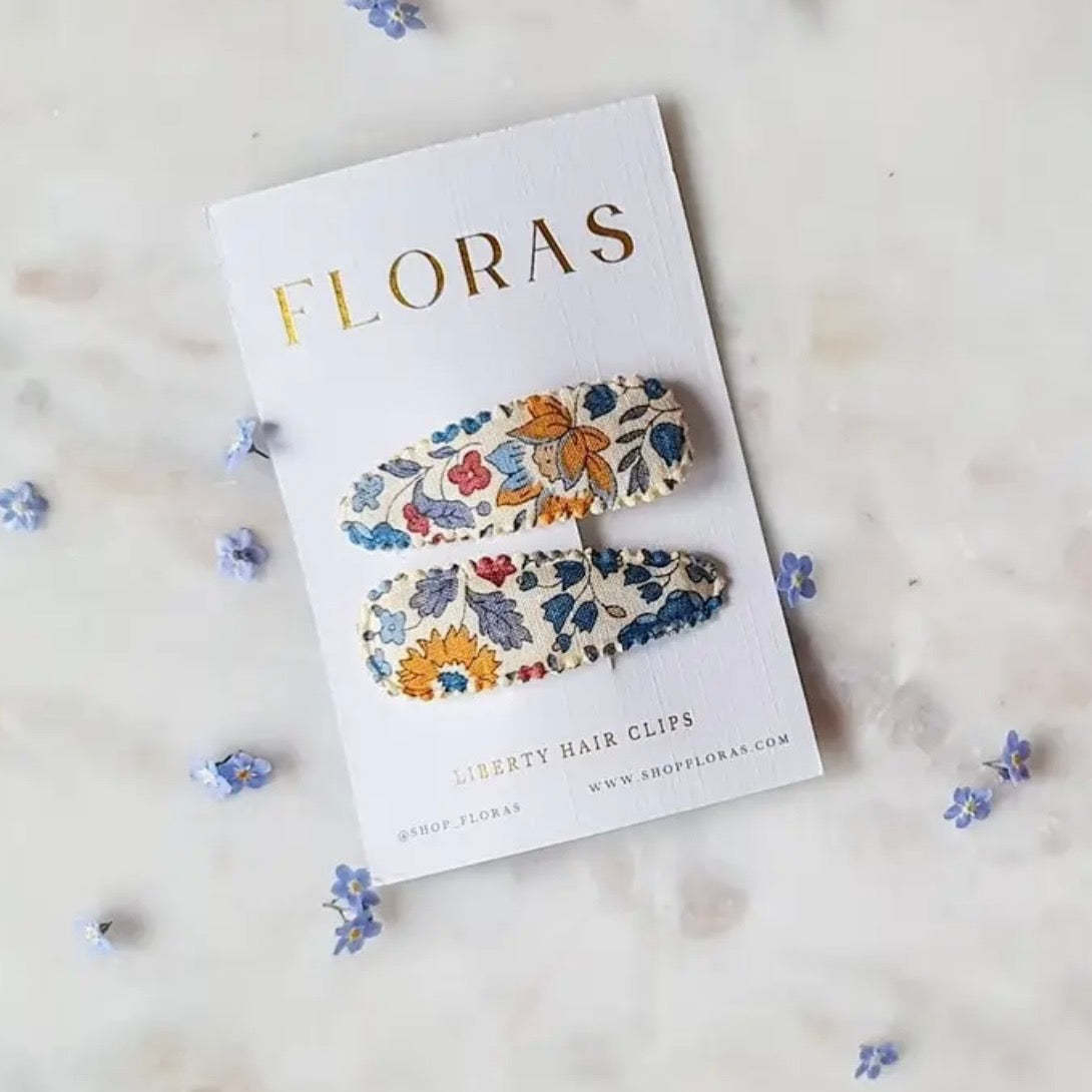 Two floral Liberty Hair Clips by FLORAS displayed on a white branded card, arranged on a light marble surface with small blue flowers scattered around.
Hair Clips
Liberty Print
Gift inspiration
Floral
Girls Hair Accessories