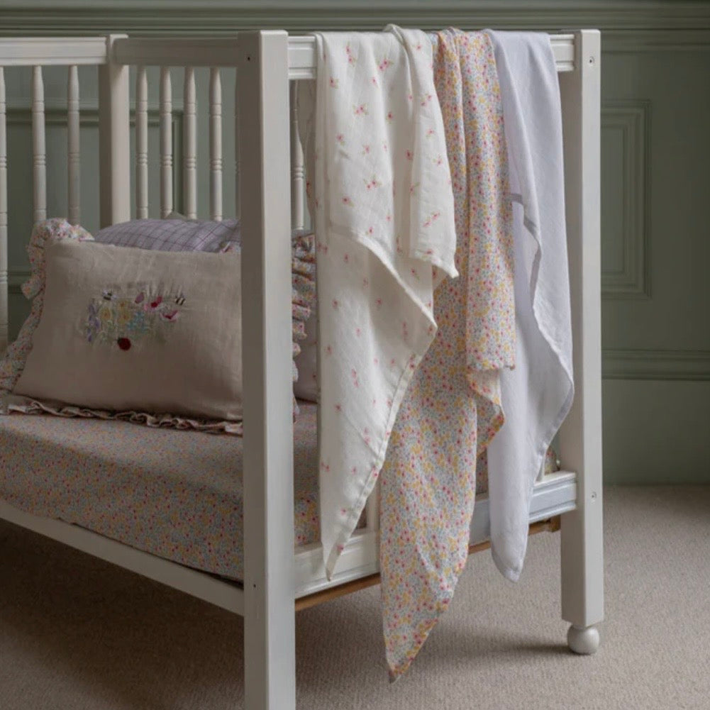 White crib with floral muslin and a decorative pillow in a neutral room.