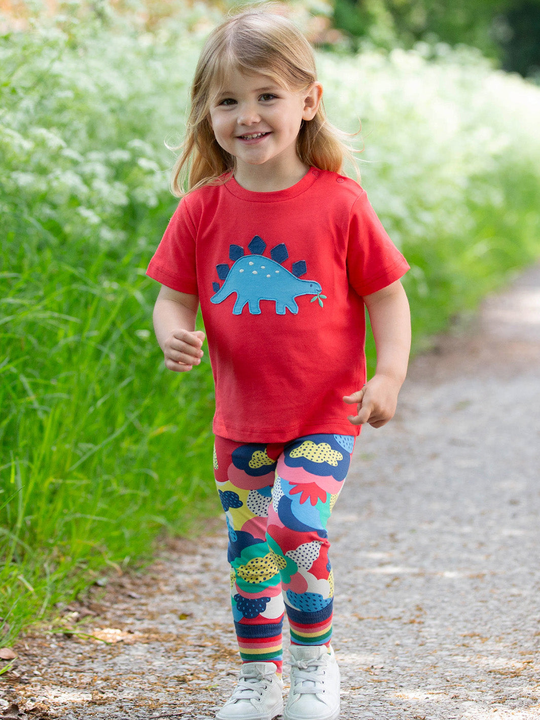 Child wearing a red shirt with a dinosaur design and colorful leggings outdoors.