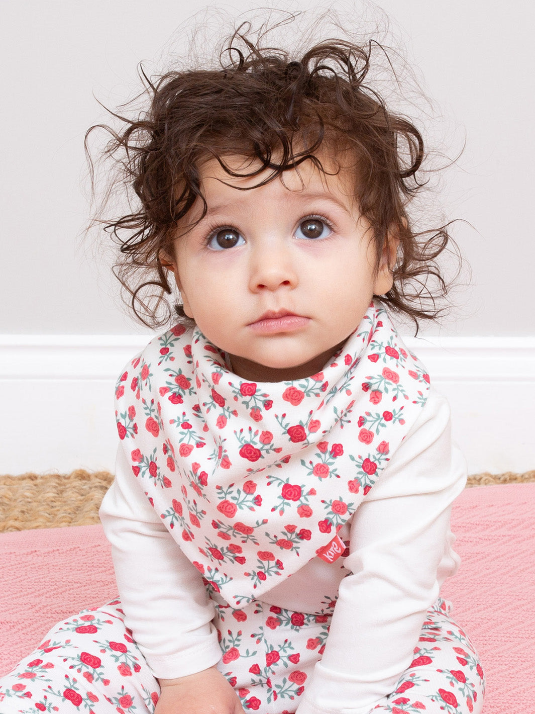 Child wearing a floral bib and outfit on a pink blanket