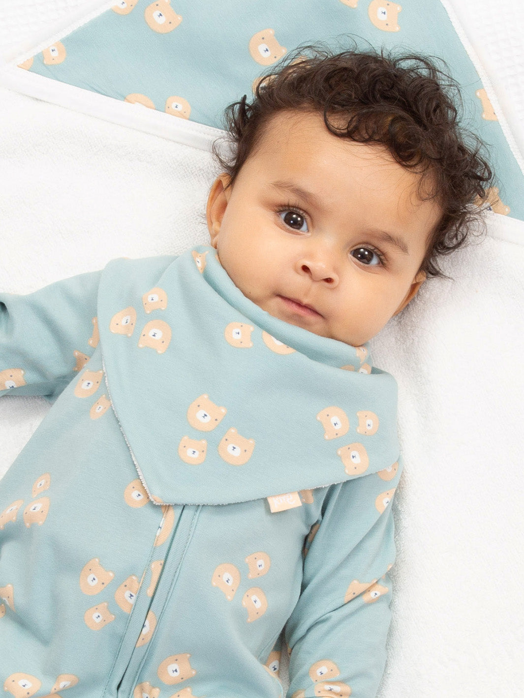 Baby wearing a light blue outfit with bear patterns on a white blanket