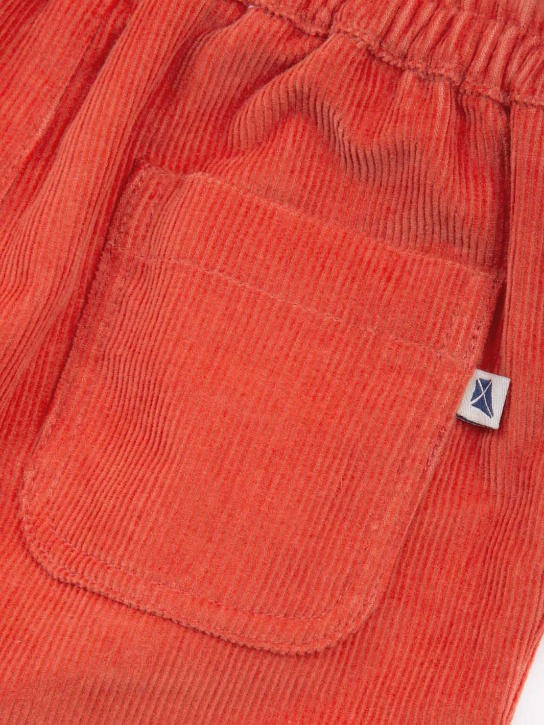 Close-up of orange corduroy trousers with a brand logo on the pocket.