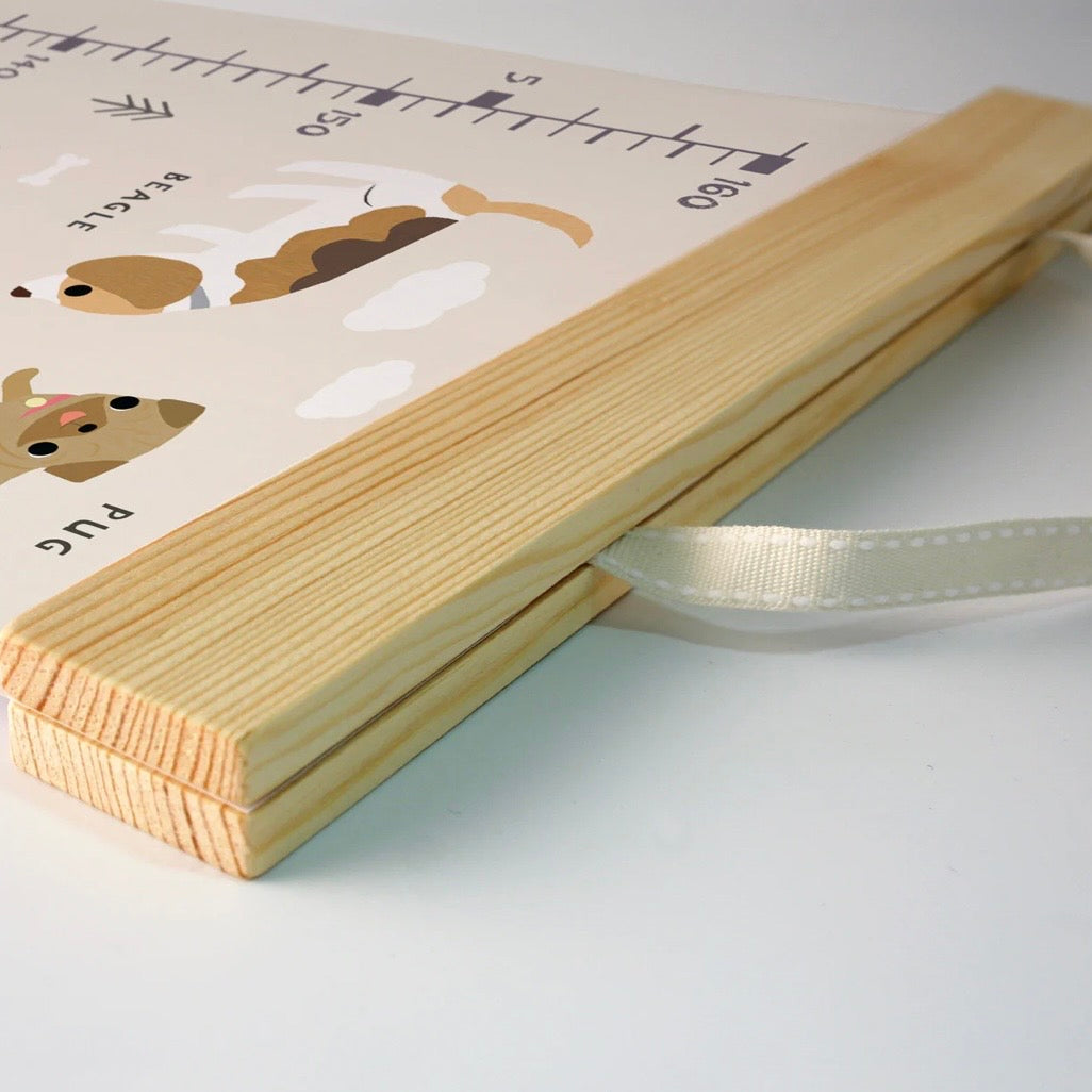 A wooden baby height chart and weight scale board with cute dog illustrations, featuring a white ribbon loop, photographed on a clean white background.

Printed in the UK
Dogs
Height chart 
Nursery decor 
James Ellis
New baby gift