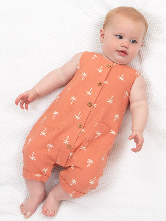 Baby wearing an orange sleeveless dungarees  with white coco tress on a white background