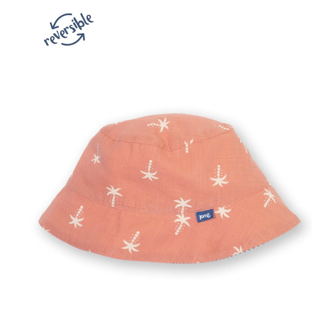 A peach-colored bucket hat with a white palm tree pattern, featuring a small blue 'petit' brand tag on the side. The image includes a 'reversible' graphic overlay in the top left corner.

Sun Hat
Children's clothing 
Children's sun hat 
GOTS Certified fabrics 
Reversible 