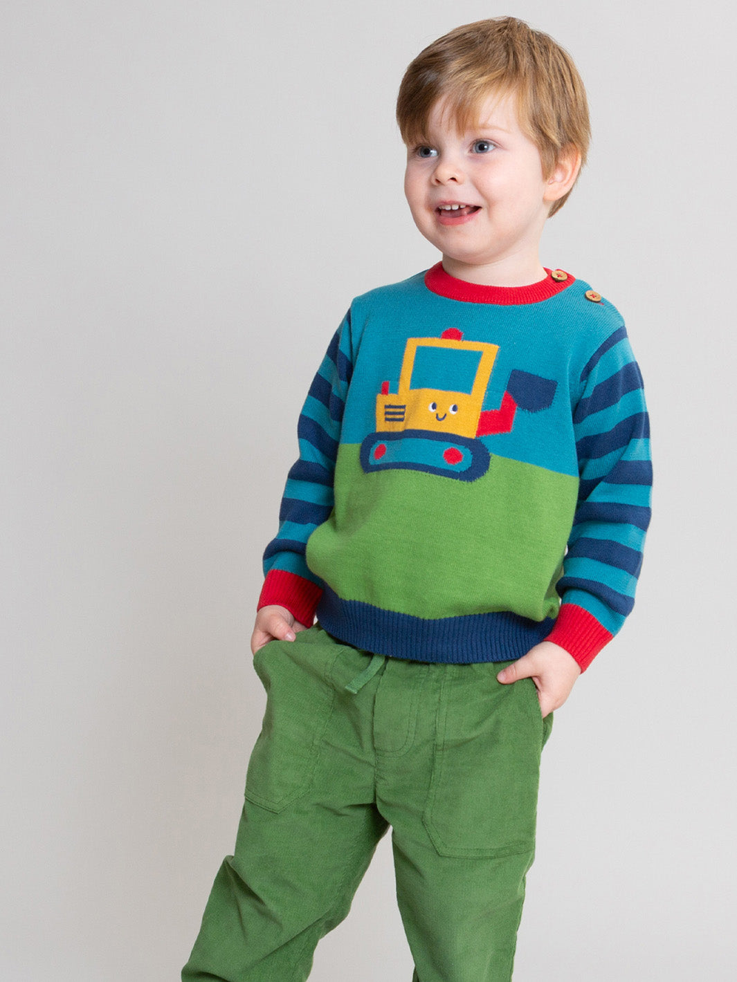 A young child wearing a colourful knit sweater with a yellow construction truck graphic and green cords, standing against a plain light grey studio background.

Olive green
Boys clothing 
Children's clothing 
Kite clothing 
Organic cotton 
Cords
Autumn clothing 