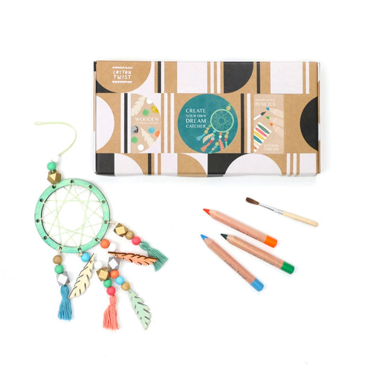 A dream catcher crafting kit is displayed, including a wooden ring, feathers, watercolor pencils, a paintbrush, beads, and string, all arranged neatly on a white background.