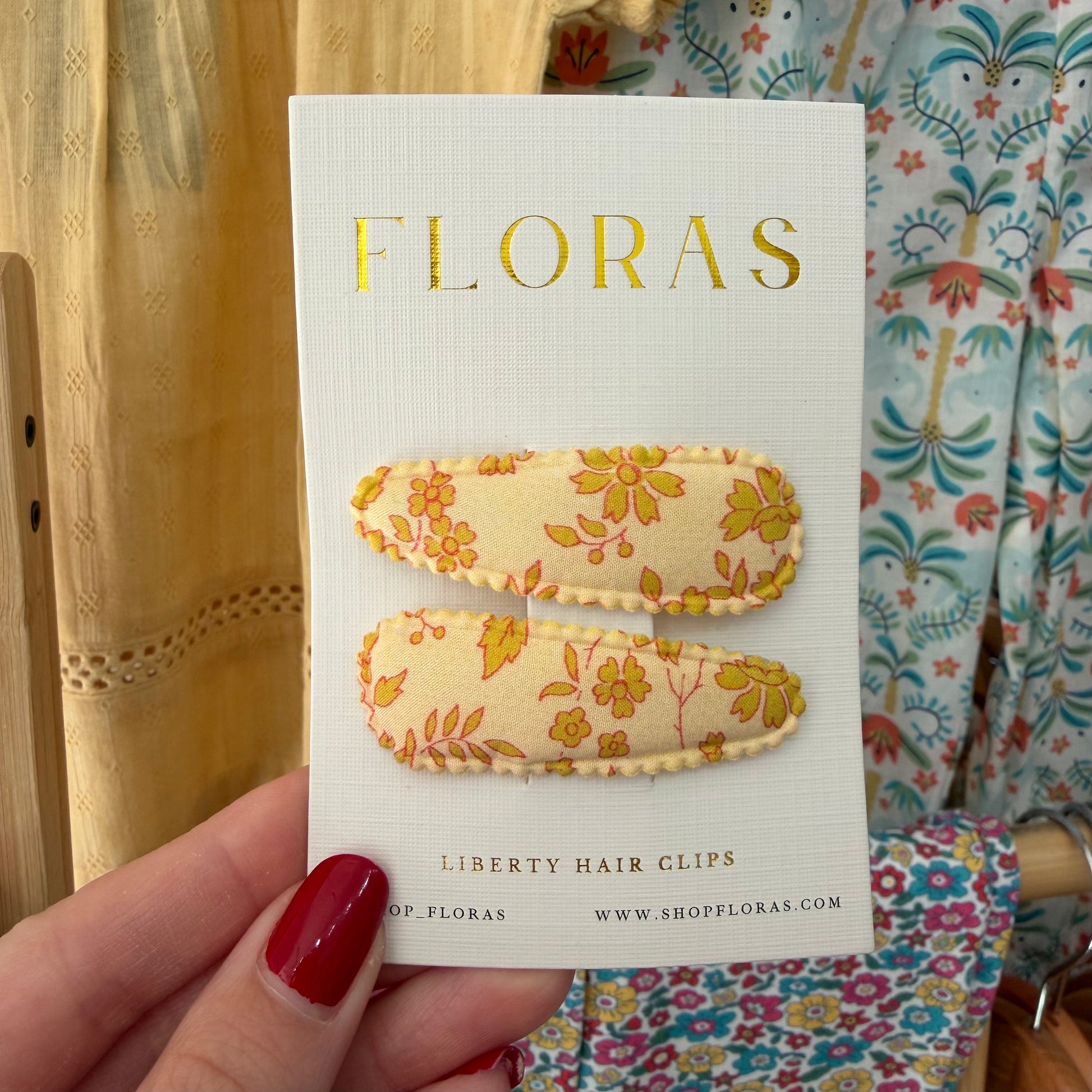 A hand with red nail polish holds a white card displaying two Liberty hair clips. The clips have a cream base with a yellow and orange floral pattern.

Hair Clips
Liberty Print
Gift inspiration 
Floral
Girls Hair Accessories