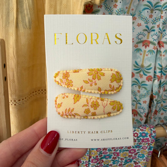 A hand with red nail polish holds a white card displaying two Liberty hair clips. The clips have a cream base with a yellow and orange floral pattern.

Hair Clips
Liberty Print
Gift inspiration 
Floral
Girls Hair Accessories