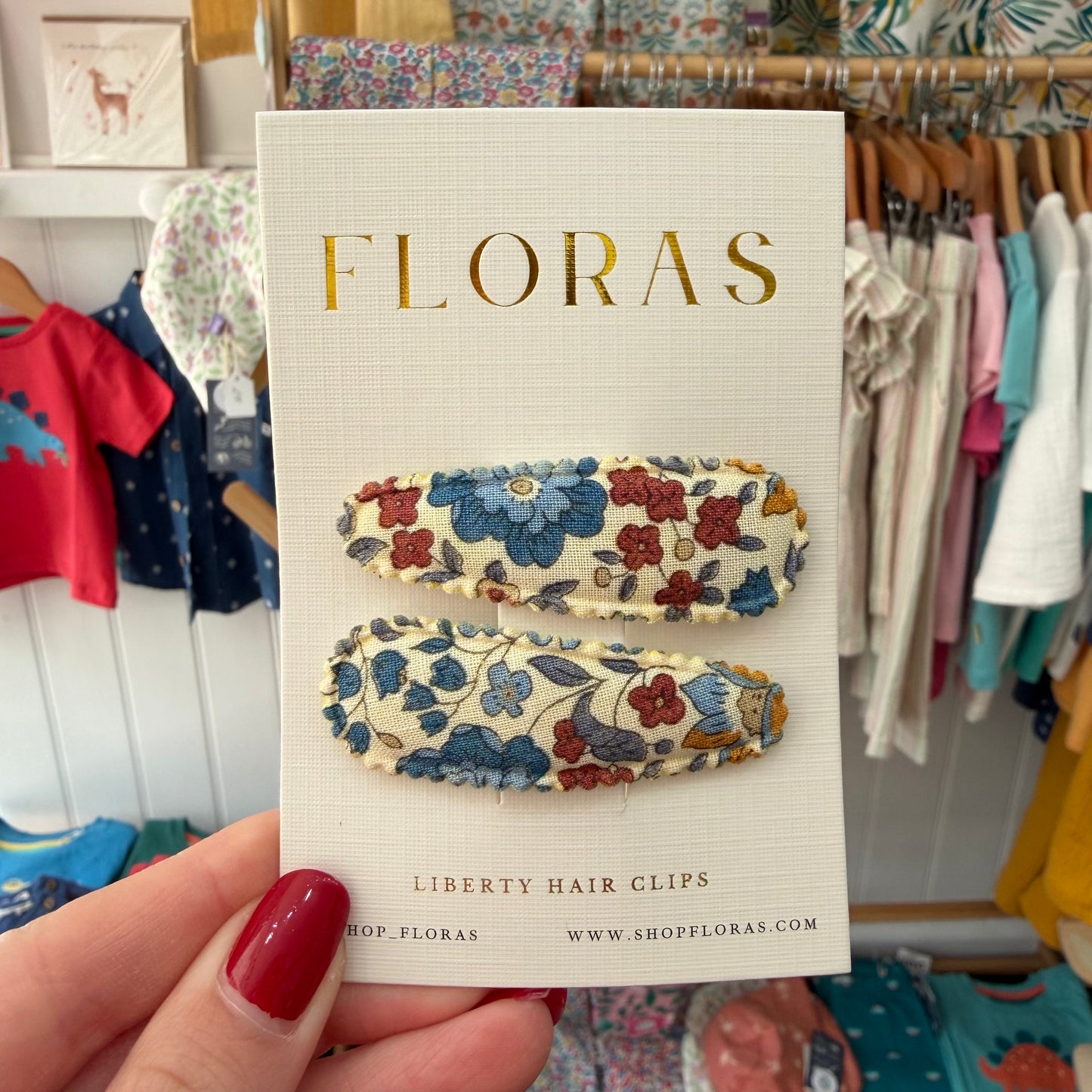 A hand with red nail polish holds a card displaying two Liberty hair clips. The clips have a cream background with blue, red, and yellow floral patterns.

Hair Clips
Liberty Print
Gift inspiration 
Floral
Girls Hair Accessories