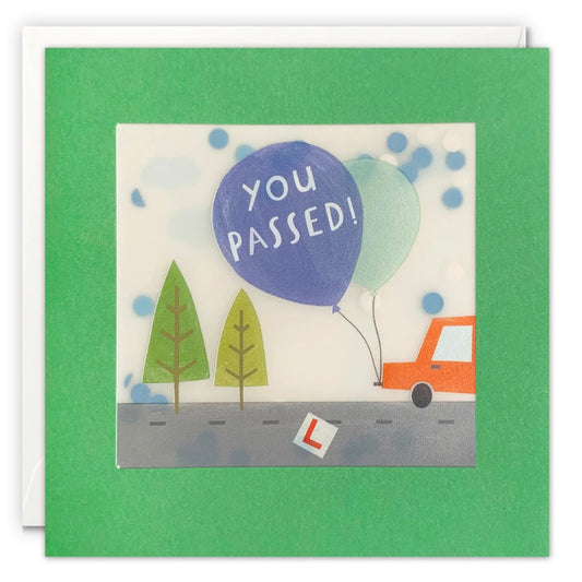 Greeting card with 'You Passed!' balloon, trees, and car on a green border