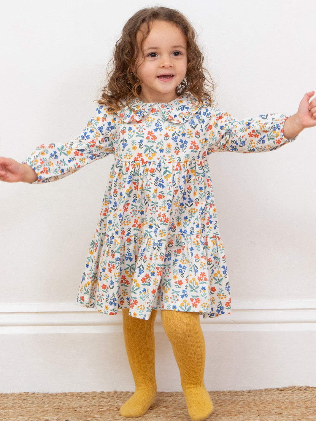 Child wearing a floral dress with long sleeves and yellow tights on a white background