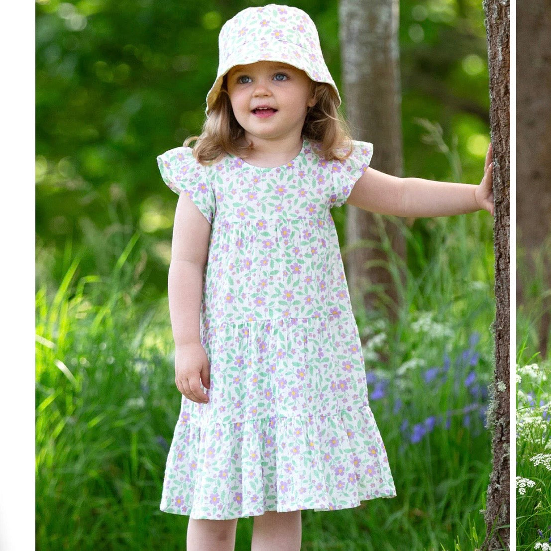 A girl wearing a white tiered dress with a pink and green floral print, a matching sun hat, and standing outdoors in a grassy garden next to a tree trunk.

Childrens hat
Sun hat 
Kids clothing 
Floral print
Reversible 