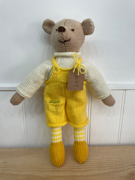 Knitted teddy bear in yellow overalls with a brown tag on a wooden surface.
Hand knitted in South Oxfordshire 