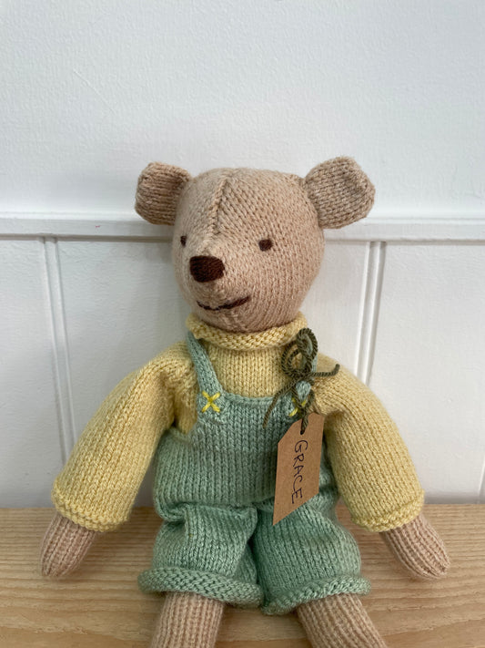 Knitted teddy bear wearing a green outfit with a white background