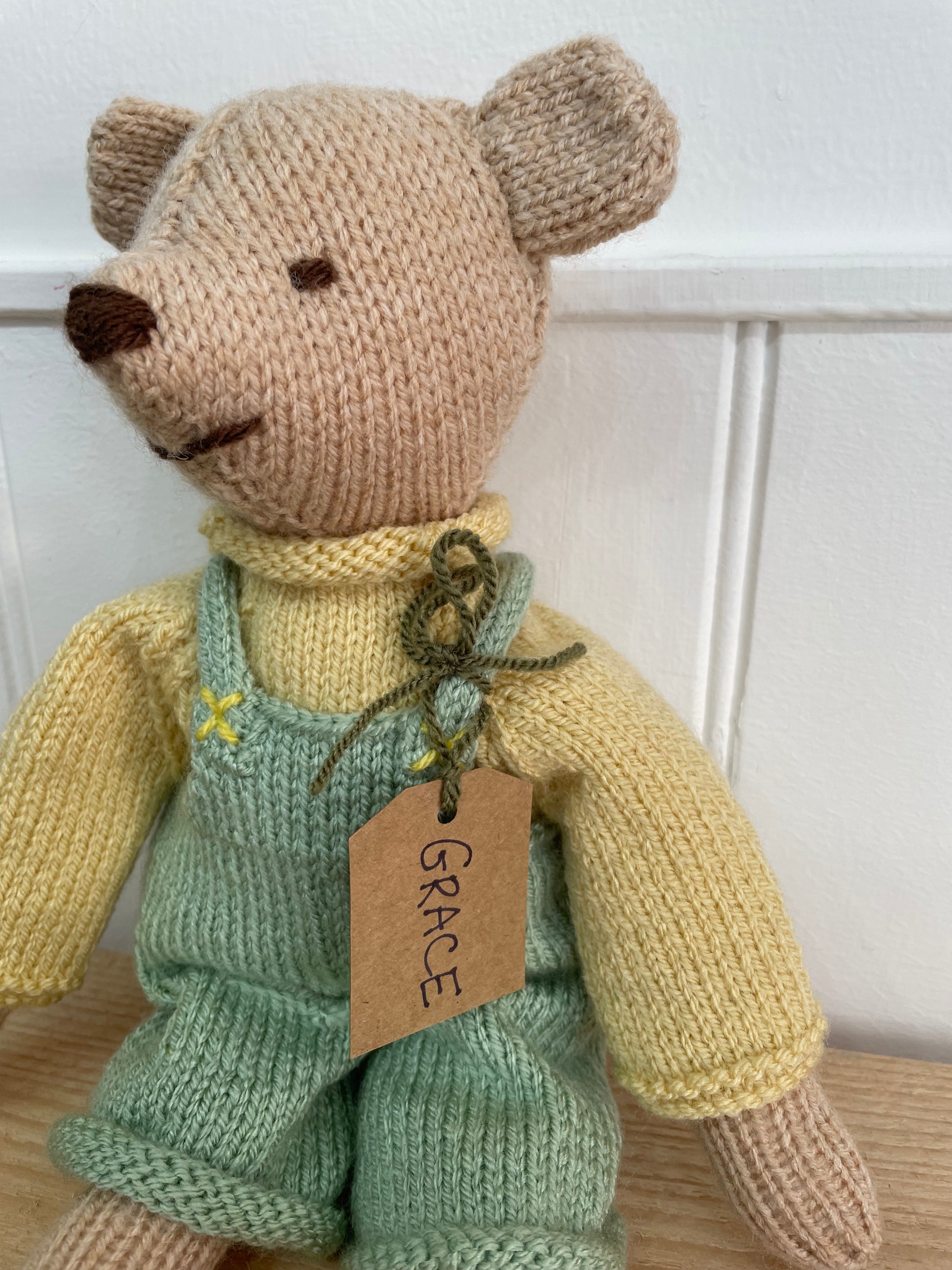 Knitted teddy bear wearing green overalls with a 'Grace' tag on a white background
Lovingly handmade in South Oxfordshire 