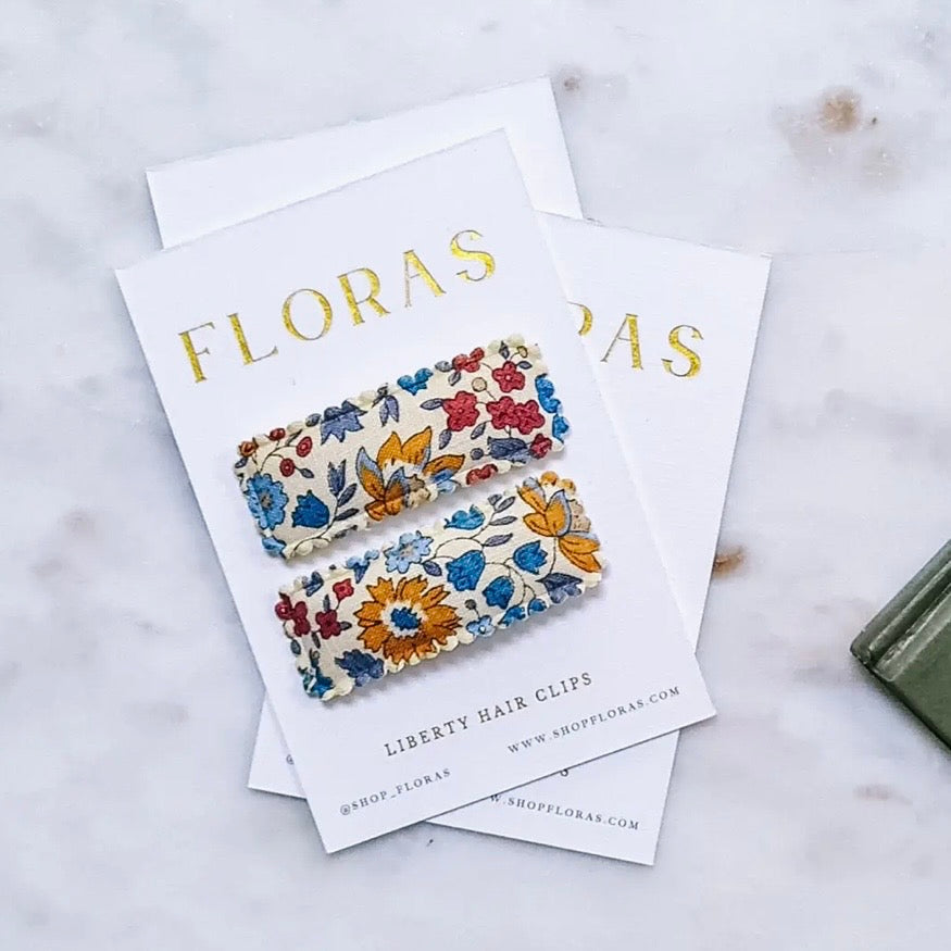 Two floral Liberty Hair Clips displayed on white cards with gold foil branding, set on a light marble surface.

Hair Clips
Liberty Print
Gift inspiration 
Floral
Girls Hair Accessories