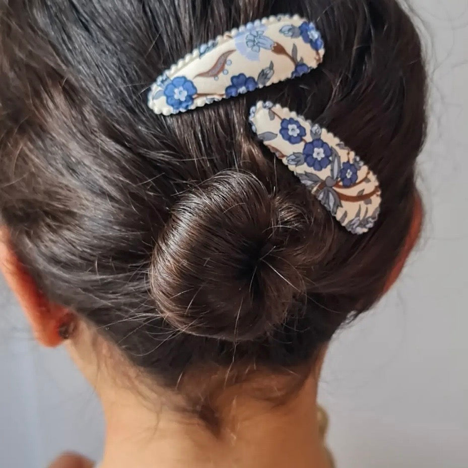 Two fabric hair clips with a blue and brown floral pattern on a cream background, shown pinned to a woman's dark hair in a low bun.

Hair Clips
Liberty Print
Gift inspiration 
Floral
Girls Hair Accessories