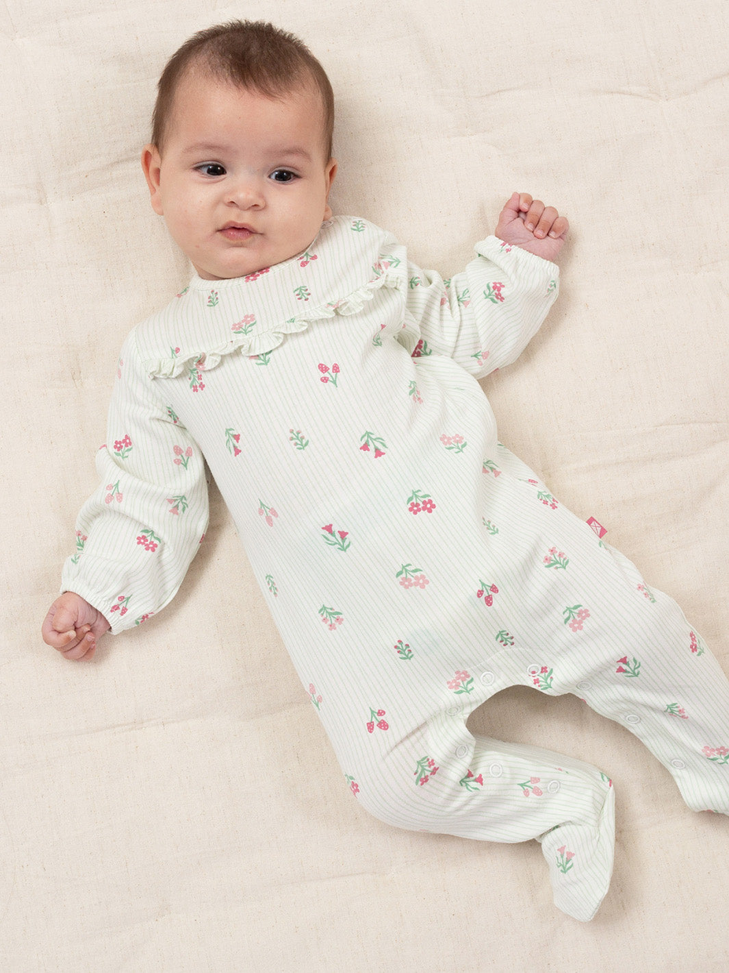 A baby lying on a cream-colored blanket, wearing a white footed long-sleeve romper with a delicate pink and green cherry pattern and a ruffled collar.

Organic cotton sleepsuit
New baby 
New baby gift
Organic cotton 
Baby clothing 
Sleepsuit
Onesie 
Baby girl
Kite Clothing
