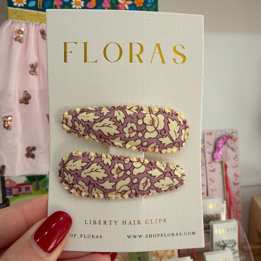 Two floral patterned hair clips on a white FLORAS display card, held by a hand with red nail polish in a store setting.

Hair Clips
Liberty Print
Gift inspiration 
Floral
Girls Hair Accessories