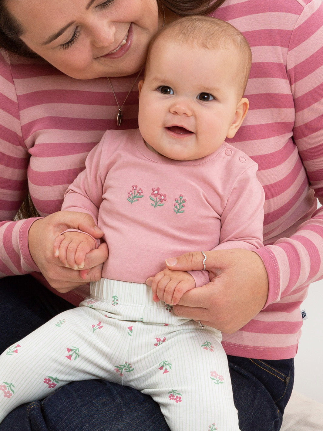 A baby wearing a pink long-sleeve bodysuit with a small floral print and white patterned pants, held by an adult wearing a pink and white striped shirt.

New baby gifts
Baby girl
Organic cotton 
Kite Clothing
Pixie Glade
Bodysuit