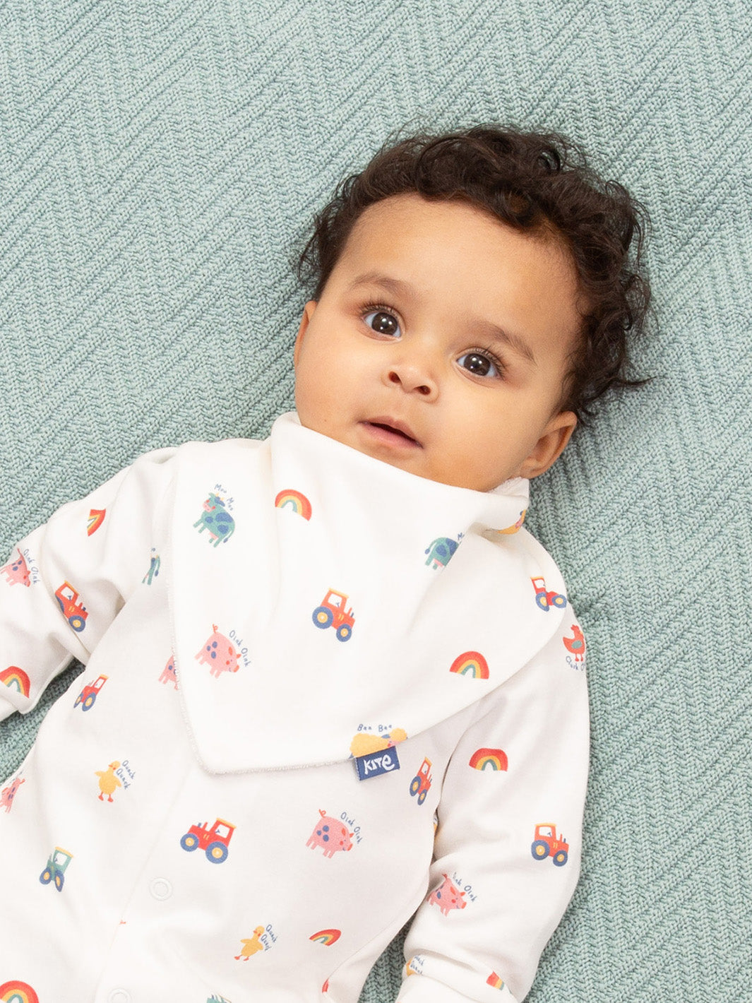 Baby wearing a white onesie with colorful patterns on a textured green blanket