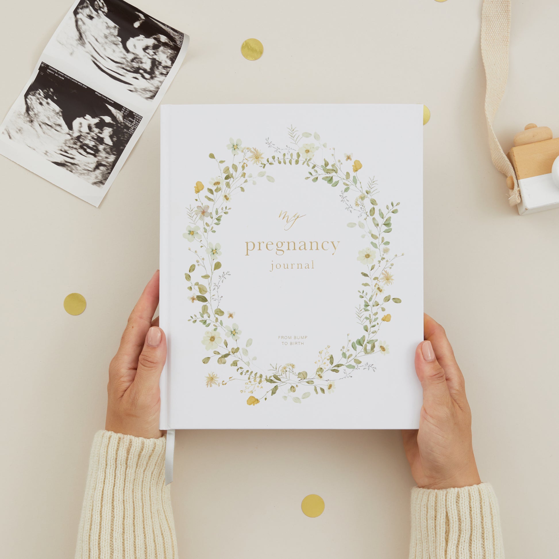 Pregnancy journal with floral design held by hands on a light background