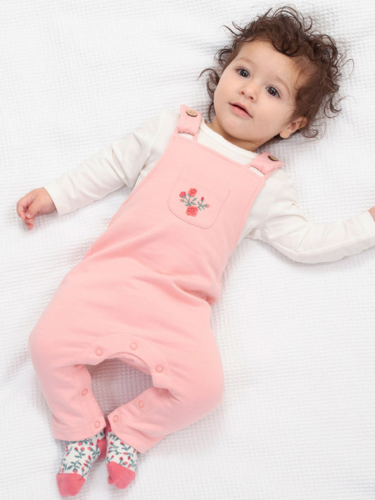 Baby wearing a pink dungaree with a floral design on a white blanket