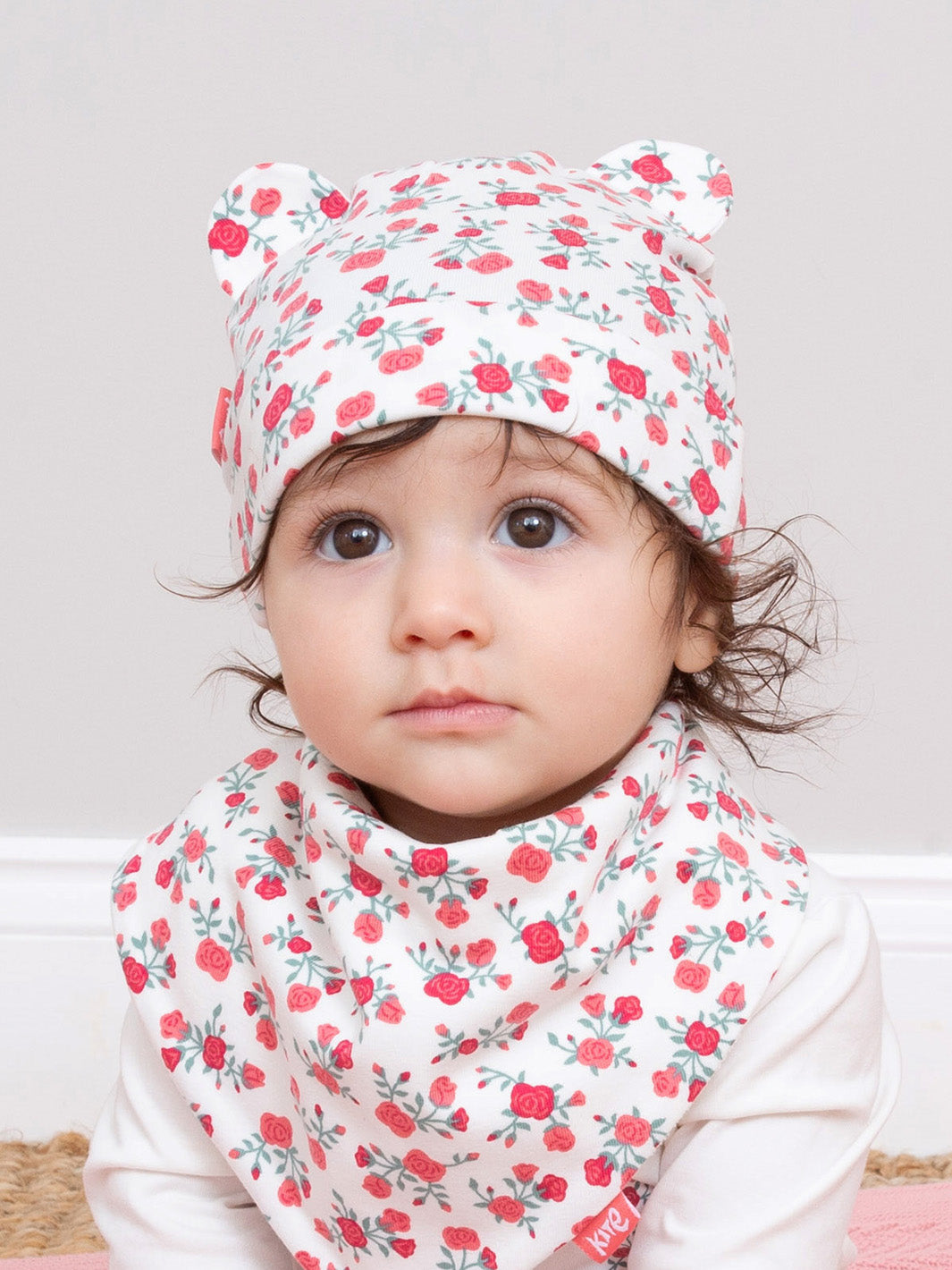 Child wearing a floral hat and bib against a light background