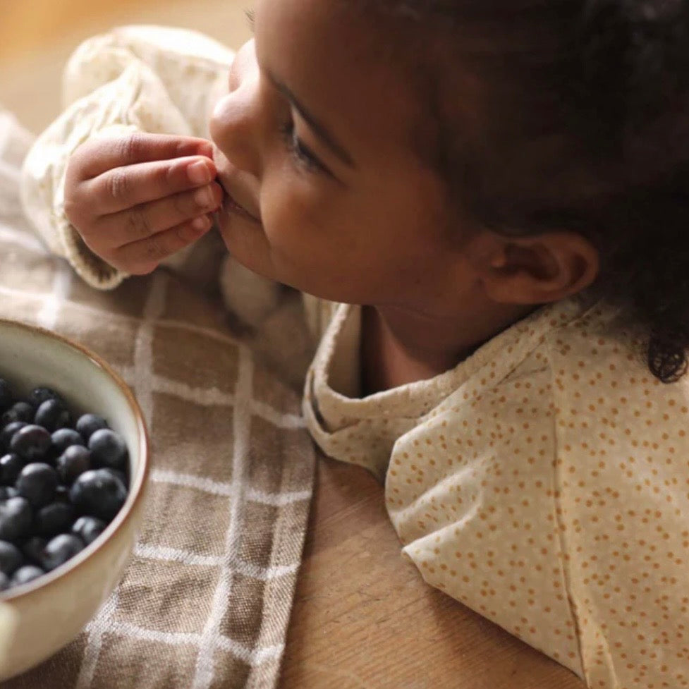 Child eating wearing our Sleeved Bib - Daisy Meadow