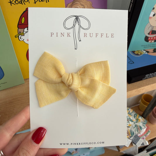 A pale yellow fabric bow attached to a white display card printed with the brand name PINK RUFFLE, held by a hand with red nail polish against a colourful background of books and stationery.

Hair Clips
Liberty Print
Gift inspiration 
Floral
Girls Hair Accessories