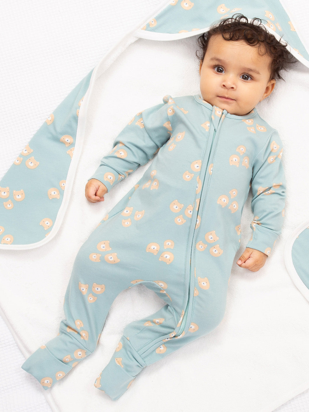 Baby in a light blue onesie with bear pattern lying on a white blanket