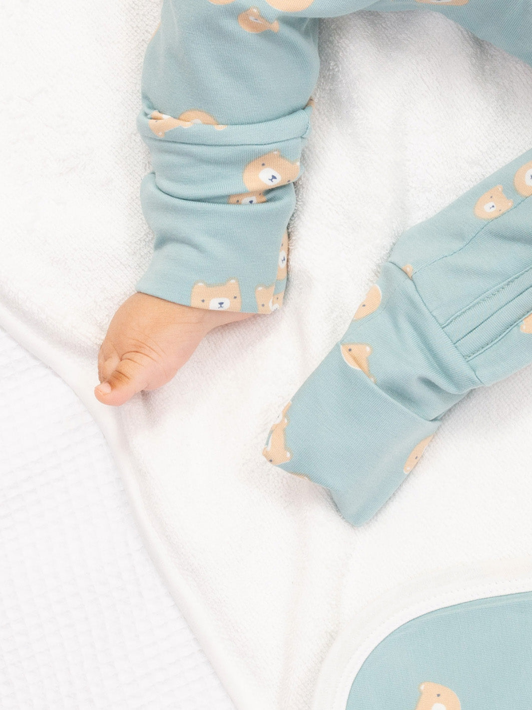 Baby's legs in light blue sleep suit with bear pattern on a white blanket