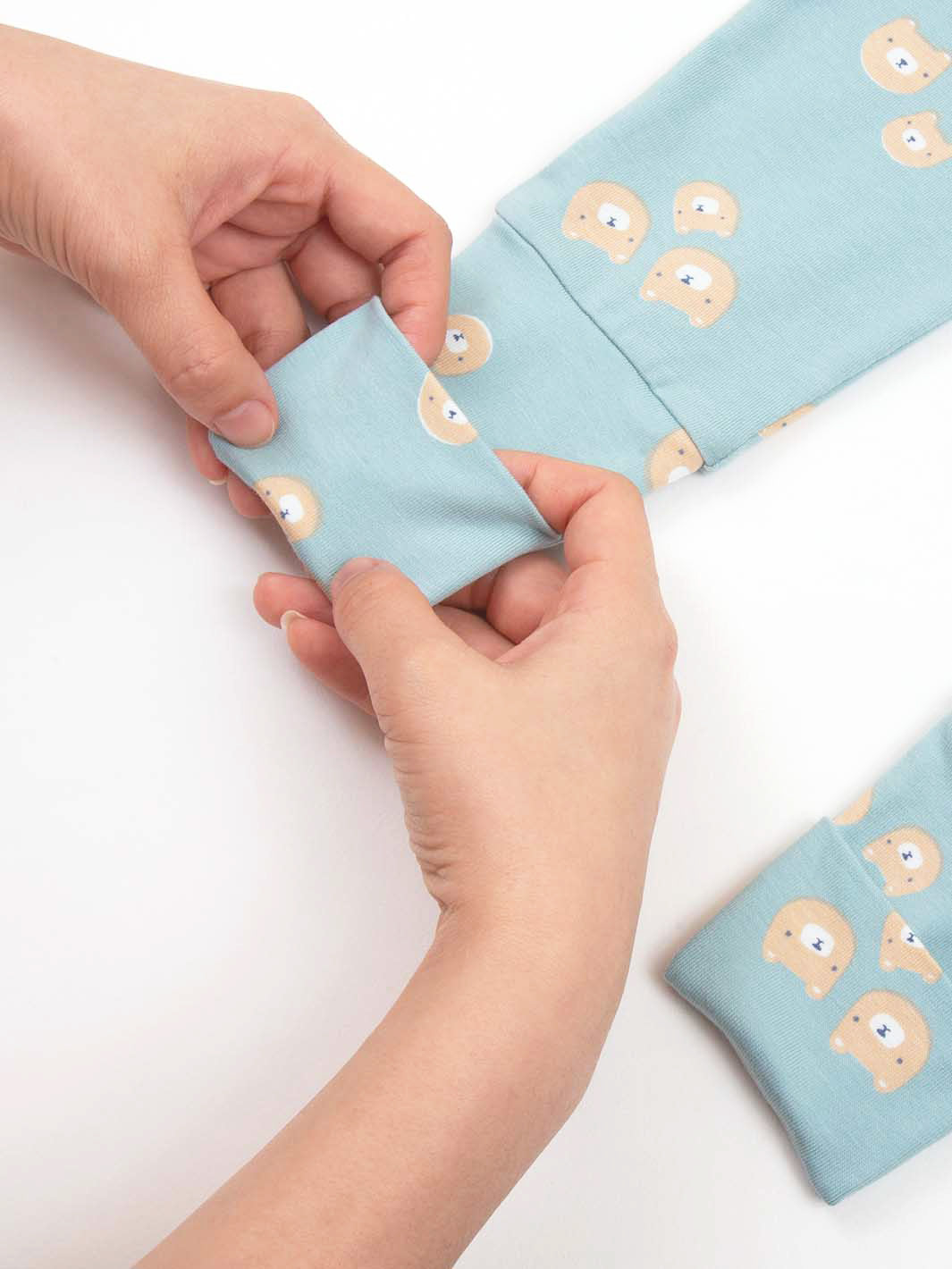 Hands holding the adaptable turn back feet on our bear pattern sleepsuit on a white background