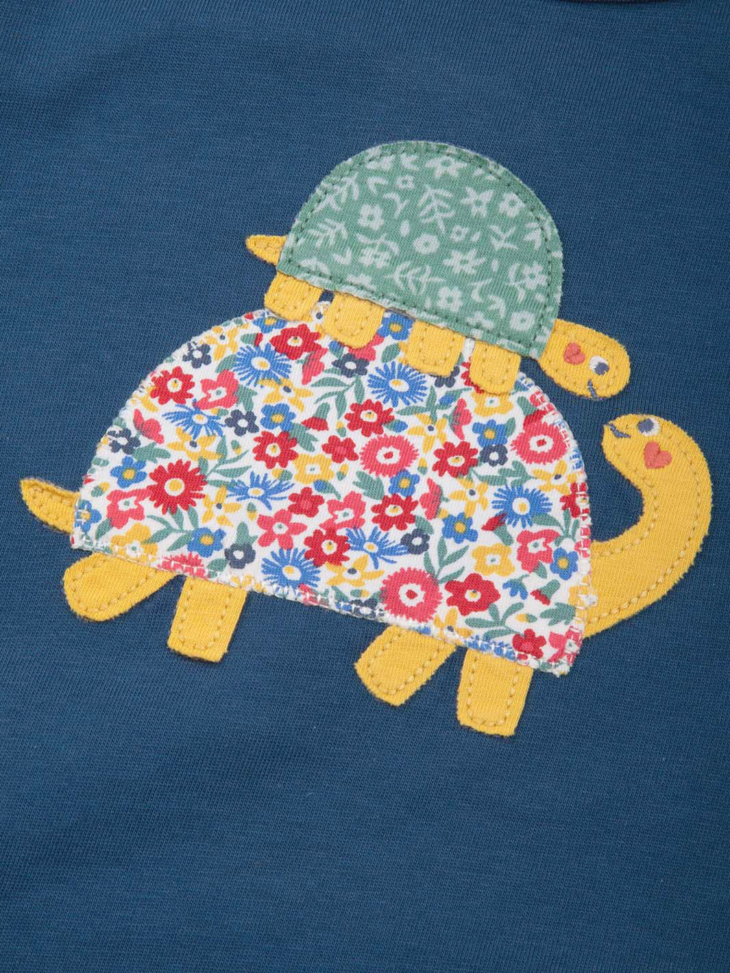 Tortoise with floral shell and green hat on a blue background. Close of appliqué 