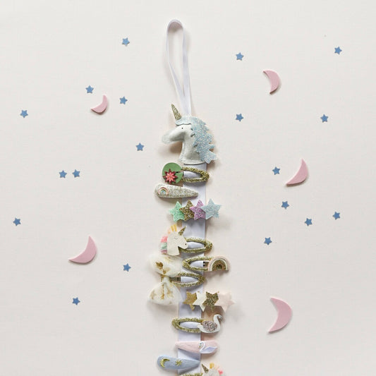 Decorative hair clip hanger in a  unicorn and star design on a light background. 
Showing what the clip hanger looks like in use