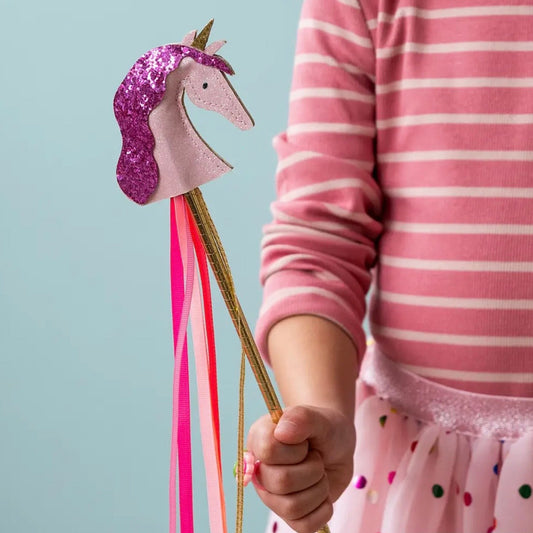 A child wearing a pink and white striped long-sleeve shirt holds a glittery unicorn wand with a pink and purple glitter head, gold horn, and pink and red ribbons against a light blue background.

stocking filler, fairy wand wholesale, magic wand toy, fancy dress accessories, role play toys, unicorn themed toys, dress up toys, party bag fillers, magical gifts, imaginative play, ribbon streamer wand