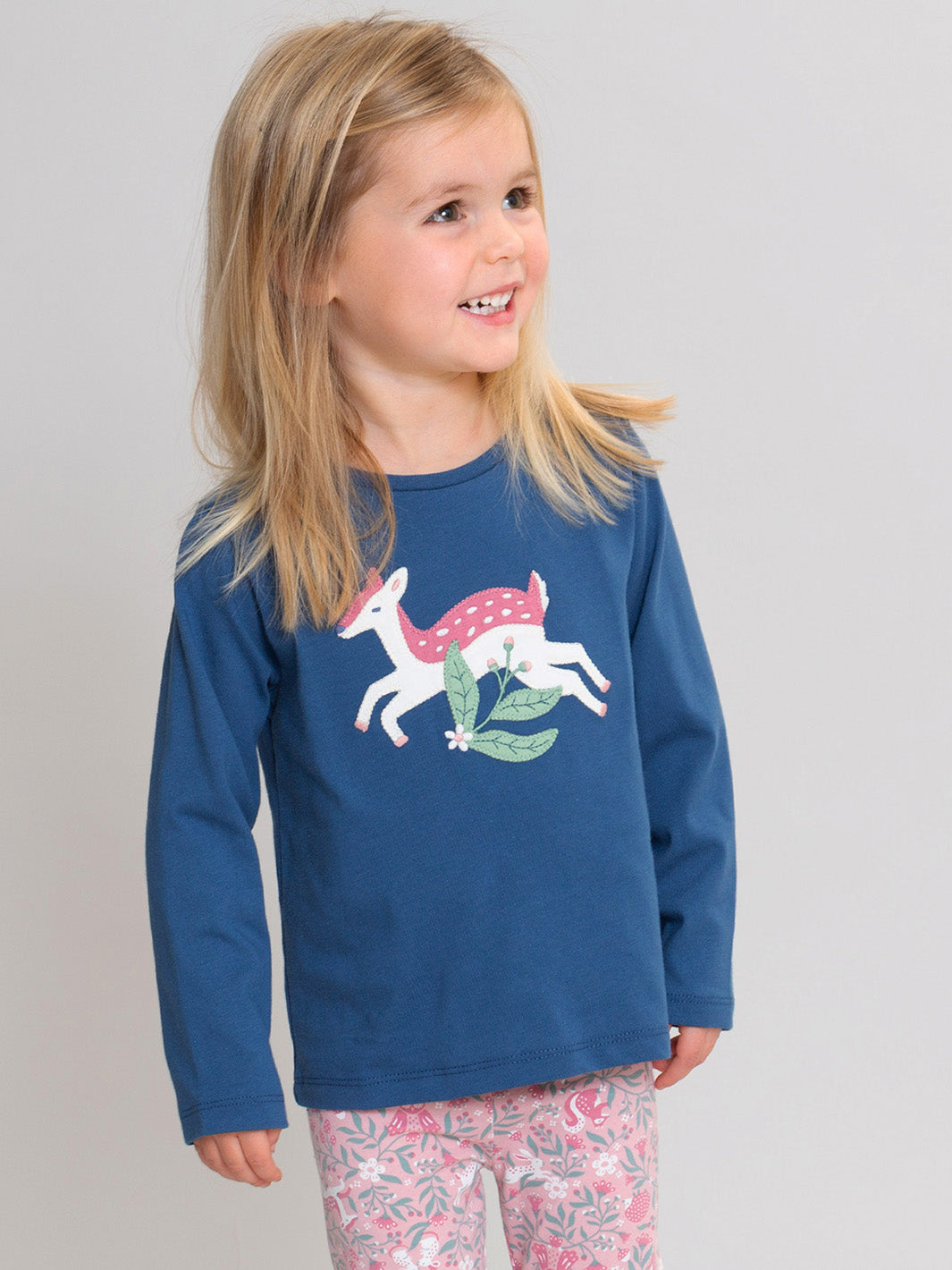 A young girl with blonde hair wearing a navy blue long-sleeve t-shirt with a white deer appliqué and pink patterned leggings, standing against a light grey studio background.

T-Shirt 
Children's clothing
Organic cotton 
Navy
Deer
Kite clothing