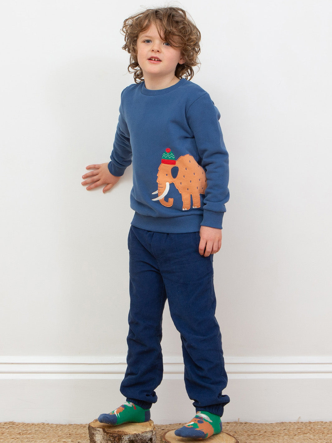 Child wearing a blue sweatshirt with a cute mammoth design and matching trousers on a white background