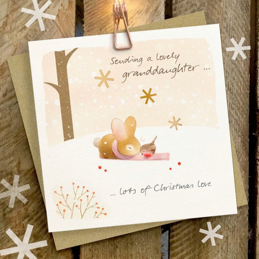 A square Christmas greeting card with a bunny and bird illustration, placed on top of a kraft envelope on a rustic wooden surface. The card reads 'Sending a lovely granddaughter .

Ginger Betty Cards
Christmas Cards
Christmas
Granddaughter 
Mouse
Robin
Printed in the UK